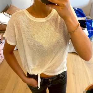 Vit knyt-topp i mesh - Vit topp med knyt framtill. Toppen har korta ärmar och rund halsringning! Materialet är tunt och ger en avslappnad vibe. Går att knyta där nere! Supercool! Passar xs-m beroende på hur man vill att den ska sitta’ 