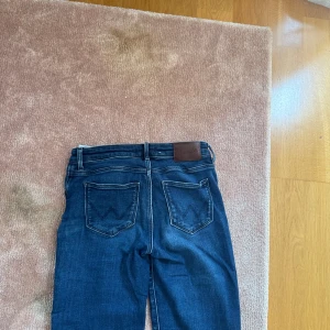 Wrangler bootcut jeans mörkblå - Mörkblå jeans från Wrangler med klassiska bakfickor och bootcut passform. Jeansen har normal midja och är tillverkade i stretchig. 25/small i midjan och jag på bilden är 171 cm lång. Dem är i väldigt bra skick och används cirka 3 gånger. Nypris:1000kr. Pris kan diskuteras.