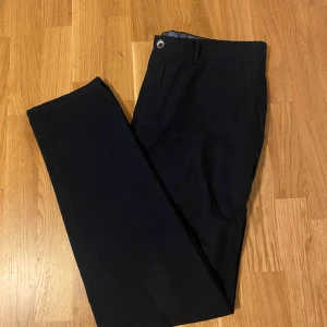 Svarta kostymbyxor Massimo Dutti - Snygga svarta kostymbyxor från Massimo Dutti i slim fit-modell. Byxorna har klassisk design med knapp och hällor i midjan, perfekta för en clean och stilren look. Materialet känns mjukt och har en elegant finish.