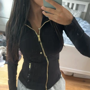 Svart jacka från Lululemon med guldzip - Snygg svart jacka från Lululemon med guldiga dragkedjor och figurnära passform. Jackan är långa ärmar och två fickor med dragkedja. Perfekt för dig som gillar sportig och stilren look. Fick den I USA från släkt men har ej använt den. ☺️pris kan diskuteras 