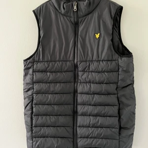Lyle & Scoot Väst - Snygg svart dunväst från Lyle & Scott med gul broderad logga på bröstet. Västen är quiltad med horisontella sömmar och har dragkedja framtill. Perfekt att slänga över en hoodie för en cool look. Använd fåtal gånger - hör av er vid frågor eller funderingar- Mvh Sigge🥂