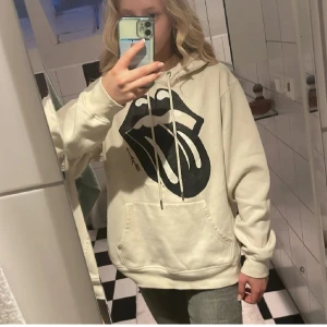 Rolling Stones hoodie från H&M - Beige hoodie från H&M med stor svart Rolling Stones-tryck framtill. Tröjan har huva med snörning, magficka och långa ärmar. Perfekt för dig som gillar  en chill och snygg stil. Skriv till mig om frågor 