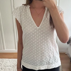 Vit broderad blus från H&M - Söt vit blus från H&M med broderade hålmönster och v-ringning. Blusen har korta ärmar med lätt volang. Den har en romantisk och luftig känsla och passar upp till strl L beroende på hur man vill att den ska sitta