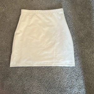 Vit kortkjol i stretchigt tyg - Enkel och stilren vit kortkjol med rak passform. Kjolen är gjord i ett stretchigt material som sitter snyggt och bekvämt. Perfekt att matcha med crop tops eller oversized tröjor för en clean look.