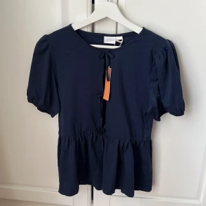 Mörkblå blus från Gina Tricot - Supersöt mörkblå blus från Gina Tricot med puffärmar och volang nedtill. Toppen har knytning framtill vid halsen. Aldrig använd, pris lapp sitter kvar🩷
