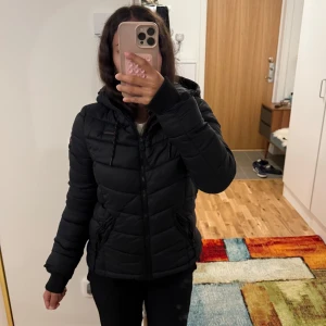 Svart pufferjacka från Marikoo - Säljer en svart pufferjacka från Marikoo med huva och dragkedja. Jackan har snygga quiltade paneler, ribbade muddar och snörning i huvan. Perfekt för kalla dagar och riktigt skön att bära. Fickor med dragkedja på sidorna. Nypris 800kr❤️