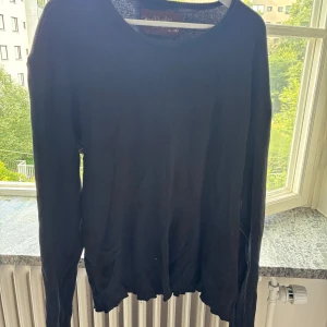 Svart ribbad tröja från Stockholm (Surfboard) Club - Svart långärmad tröja från Stockholm (Surfboard) Club i storlek 2XL. Tröjan är ribbad och tillverkad i 100% ekologisk bomull. Enkel och clean design med rund hals och relaxed fit, perfekt för dig som gillar en stilren look.