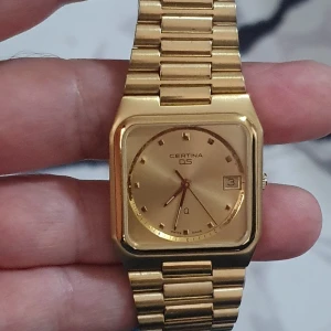 Guldig Certina DS herrklocka - Stilren Certina DS herrklocka i helguldigt utförande med fyrkantig boett och länkarmband i metall. Urtavlan är guldig med datumvisning och diskreta indexmarkeringar. Klassisk och tidlös design som sticker ut på handleden mycket fint skick som ny har ny batteri obsss det är äkta certina swiss made