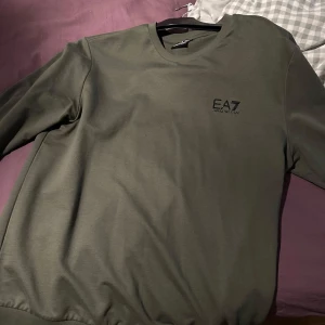 Olivgrön EA7 crewneck tröja - Snygg olivgrön crewneck från EA7 Emporio Armani med diskret logga på bröstet. Använd kanske 1 eller 2 gånger för liten för mig därför jag säljer den