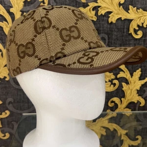 Gucci beige keps - Snygg keps från Gucci i beige och brunt med det klassiska GG-mönstret över hela kepsen. Justerbar rem bak i brunt skinn och böjd skärm med läderkant. Perfekt för dig som vill sticka ut med en lyxig accessoar.