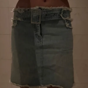 Ljus jeanskjol med råa kanter och bälte - Säljer en ljusblå jeanskjol med råa, fransiga kanter och ett brett bälte i midjan. Kjolen har en rak passform och är perfekt för dig som gillar en edgy och avslappnad stil. Enkel att matcha med crop tops eller hoodies.