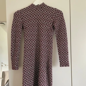Mönstrad långärmad klänning Topshop - Säljer en långärmad klänning från Topshop i storlek 34. Klänningen har ett tätt, geometriskt mönster i vinrött, svart och vitt, hög hals och dragkedja i ryggen. Modellen är figurnära och tyget känns mjukt och stretchigt och är en kort klänning. Kan skicka fler bilder☺️