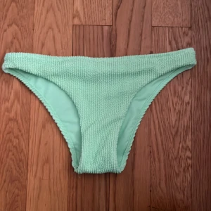 Ljusgrön bikiniunderdel - Säljer en ljusgrön bikiniunderdel i ribbat material. Bikinin har en enkel och klassisk form med medelhög midja och är tillverkad i stretchigt tyg för bekväm passform. Materialet består av 93% polyester och 7% elastan. Perfekt till stranden eller poolen.