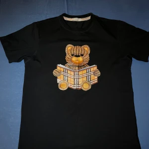 Burberry T-shirt Svart - Säljer en svart Burberry t-shirt i storlek S. Passar även M då den har en något rymlig passform. Klassisk och stilren design med Burberrys kvalitet i både material och detaljer. Väldigt sparsamt använd och i mycket bra skick – inga fläckar, hål eller märken. Tyvärr finns inget kvitto kvar eftersom tröjan var en present, men äktheten kan ses på material, sömmar och detaljer.