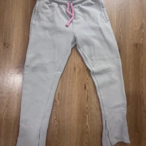 Ljusgrå mjukisbyxor från Syna world - Ljusgrå mjukisbyxor från Syna world med rosa dragsko i midjan och tryck i rosa på baksidan. Byxorna har resår i midjan och är tillverkade i mjuk bomullsblandning. Perfekta för en avslappnad stil. Jag säljer dessa byxor eftersom jag vill vara behålla hoodien då den kom i tracksuit. Jag har använt dessa byxor 2 gånger. Pris kan snackas vid snabba affärer