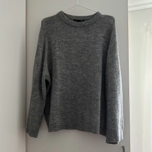 Grå stickad tröja  - Mysig grå stickad tröja med rund halsringning och långa ärmar. Perfekt för kyliga dagar och enkel att matcha med olika outfits. Klassisk och tidlös modell som passar till det mesta.