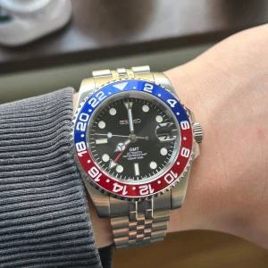 Seikomod GMT klocka med Pepsi-bezel - Säljer en Seikomod GMT herrklocka med svart urtavla, röd och blå vridring samt datumvisning. Klockan har rostfri länk och transparent baksida som visar urverket. Perfekt för dig som gillar sportig stil och klassisk design. Inuti sitter ett Nh34 urverk från Seiko. Klockan är vattentät och har lume som gör klockan läsbar i mörkret. Skicka dm vid frågor eller prisförslag 😁📩