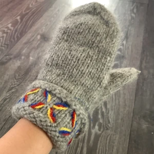 Grå stickade vantar med broderi - Handgjorda grå stickade vantar med färgglatt broderi i rött, gult och blått vid mudden. Perfekta för kyliga dagar och ger en mysig känsla. Klassisk tumvante-modell.