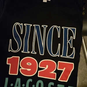 Svart t-shirt från Lacoste LIVE med tryck fint skick Stl L  - Lacoste fint skick. Stl L Normal passform. Stort tryck fram.  Endast testad. Nypris 799 kr.  