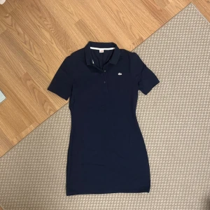 Marinblå klänning från Lacoste - Säljer en klänning från Lacoste i storlek m med klassisk krage och korta ärmar. Helt oanvänd 