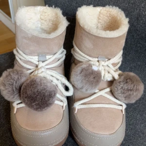 Beige vinterboots med pälsbollar från Inuikii - Säljer ett par beige vinterboots från Inuikii med fluffigt foder och stora pälsbollar framtill. Skorna har grov snörning och en platt sula med bra grepp.  Selling because the size was too small for me, bought it off vinted and Condition is good. Been used 10-20 times but in very good condition in my opinion. Size 38. The balls can be taken off or keep them