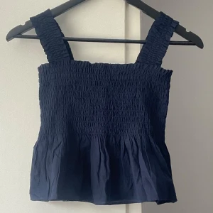 Uniqlo linne smock topp - Marinblått linne/topp med smock-detaljer från Uniqlo. Storlek S. Peplum-passform. Helt nytt, lapp kvar.