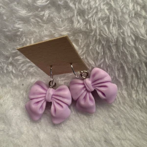 Ljuslila rosettörhängen - Säljer ett par söta örhängen formade som rosetter i ljuslila färg. Perfekta för att ge din outfit en gullig och lekfull touch. Hängs på örat med silvriga krokar. Krokarna är i sterling silver 