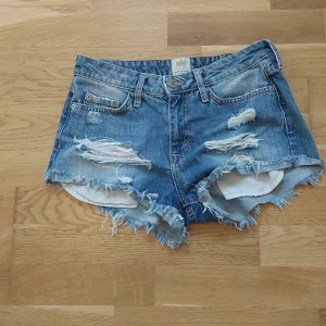 Blå jeansshorts med fransar och slitningar - Säljer ett par blå jeansshorts med råa fransar och slitna detaljer framtill. Helt nyköpta men passade tyvärr inte mig.