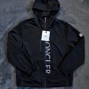 Moncler jacka - Säljer en svart vindjacka från Moncler med huva och dragkedja framtill. Perfekt till blåsiga dagar. Helt ny med tags, skick 10/10, storlek XL men passar L, pris går att diskutera✅