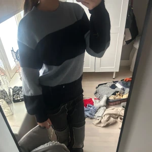 Randig stickad tröja i blått och svart - Säljer en stickad tröja med breda horisontella ränder i ljusblått och mörkblått. Tröjan har rund halsringning och långa ärmar. Perfekt för dig som gillar en avslappnad och stilren look.