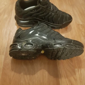 Nike Air Max Plus Tn helsvarta sneakers - Säljer ett par helsvarta Nike Air Max Plus Tn sneakers med klassisk vågig design och synlig luftdämpning i sulan. Skorna har snörning och är tillverkade i en kombination av syntet och mesh för bra andningsförmåga.
