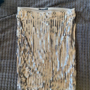 Glittrig paljettkjol från Gina Tricot - Säljer en snygg glittrig kjol från Gina Tricot i beige med massor av paljetter. Kjolen är rak i modellen och har en tight passform. Perfekt för dig som vill sticka ut med en riktigt festlig look.