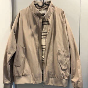 Bomberjacka från NN07 - Säljer en beige bomberjacka från NN07 med snyggt rutigt innertyg. Jackan har dragkedja framtill, två snedställda fickor och ribbade muddar vid ärmslut och nederkant. Perfekt för såväl vår och höst som en lite kyligare sommardag. Använd 1 gång och därmed i nyskick. Tror nypris låg på 3500kr, säljer för 1800kr. Jag är 185cm lång och normalbyggd och denna passar perfekt. 