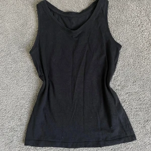 Svart linne från Lindex - En enkel och stilren svart linnetopp från Lindex. Toppen är ärmlös med rund halsringning och har en figurnära passform. Perfekt att matcha med jeans eller kjol för en clean look.