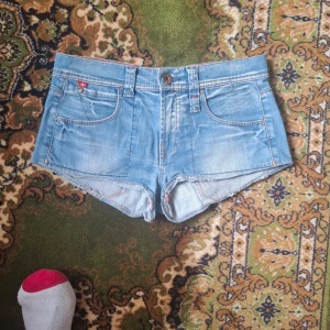 Ljusblå jeansshorts från Levi's - Säljer ett par ljusblå jeansshorts från Levi's med klassisk femficksdesign och knappgylf. Shortsen är riktigt korta och har låg midja. Perfekta för varma sommardagar!