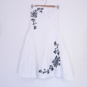 Axelbandslös klänning - KDK London strl M - Axelbandslös klänning med broderade detaljer, underkjol med tyll i kanten. Slutar precis ovanför knäna på mig som är 165cm. Öppnas med dragkedja bak. Stretchig längst upp, passar bäst dig med lite större byst. 72cm runt midjan. Kan ta fler bilder och mått vid intresse! 