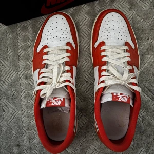 Nike Air Jordan 1 Low OG Starfish custom  - Säljer ett par Nike Air Jordan 1 Low OG i rött och vitt. Skorna har klassisk låg siluett, vit bas med röda paneler och vit swoosh på sidorna. Tjock vit sula med röd yttersula och snörning framtill. Perfekta för dig som gillar streetwear och sneakers.