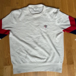 Soft goat tröja - Vit stickad tröja i 100% kashmir från Soft Goat. Tröjan har långa ärmar med breda ränder i rött och mörkblått på ärmarna samt ett broderat snöflingemärke på bröstet. Den är i strlk S.                                                                        Pris kan sänkas vid snabb affär