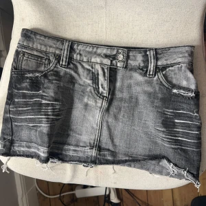 Grå mini jeans kjol med låg midja - Lågmidjad jeans kjol med dekorativa svarta pärlor på bakfickorna som formar ett M. Perfekt för dig som gillar edgy streetstyle. Blixtlåset är sönder 