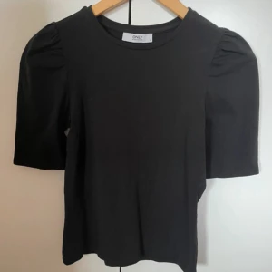 Svart topp med puffärm från ONLY - Svart topp från ONLY med rund halsringning och korta puffärmar. Enkel och stilren design som passar till många olika outfits. Tillverkad i mjukt material för en bekväm känsla.