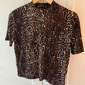 Leopardmönstrad topp från Zara - Säljer en snygg leopardmönstrad topp från Zara. Toppen har korta ärmar och en rak passform, lite polo. Superenkel att styla till både jeans och kjol! Använd vid något tillfälle. Inga tecken på användning 