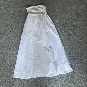 Vit långklänning från Gina Tricot - Säljer en vit axelbandslös långklänning från Gina Tricot i storlek XXS. Klänningen har en enkel och stilren design med utsvängd kjol och stretchig överdel. Perfekt för sommarens alla tillfällen!