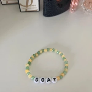 Pärlarmband med texten GOAT - Fint armband med små pärlor i grönt, gult och vitt. Armbandet har vita bokstavspärlor som bildar ordet GOAT. Perfekt accessoar för att ge din stil en personlig touch. Hov1 inspirerat 💕