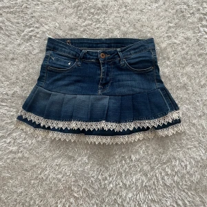 Jeanskjol med spetsdetaljer - En lågmidjad jeanskjol omsydd från ett par jeans. Midjemått tvärsöver - ca 34cm Längd - 32cm