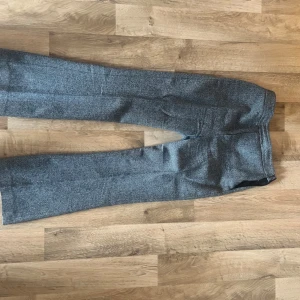 Grå kostymbyxor från Massimo Dutti - Snygga grå kostymbyxor från Massimo Dutti i klassisk rak modell. Byxorna har diskret fiskbensmönster och är perfekta till en dressad look. Tillverkade i ett mjukt material som känns bekvämt hela dagen.