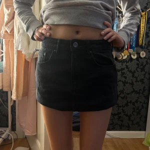 Svart minikjol i jeans - Säljer en svart lågmidjad jeanskjol med klassisk femficksdesign och knapp framtill. Kjolen har en rak passform och är perfekt för dig som gillar en enkel och stilren look.