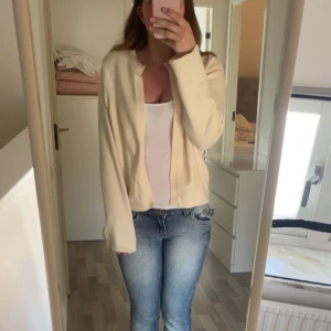 Krämvit kofta från Gina Tricot - Säljer en krämvit kofta från Gina Tricot i mjukt stickat material. Koftan har rund halsringning, lång ärm och stängs med en knapp upptill. Perfekt att slänga över en topp eller linne. 