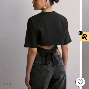 Svart topp med knyt i ryggen - Trendig svart croppad topp med korta ärmar och snygg knytning i ryggen. Perfekt för att skapa en cool och stilren look. Toppen har en enkel design utan mönster och passar till många olika outfits.