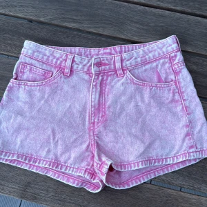 Rosa jeansshorts från Monki - Säljer ett par ljusrosa jeansshorts från Monki med klassisk femficksdesign och bälteshällor. Shortsen har normal passform och är tillverkade i bomull. Köpta i sommar och nästan aldrig använt!
