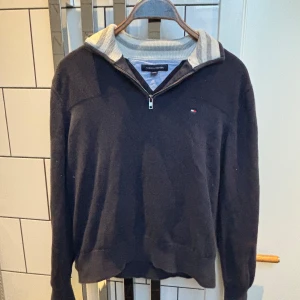 Mörkblå halvzip tröja från Tommy Hilfiger - Säljer en mörkblå stickad halvzip tröja från Tommy Hilfiger med liten broderad logga på bröstet. Tröjan har ribbad krage med gråa ränder och dragkedja framtill. Perfekt för en stilren och avslappnad look. Pris kan diskuteras.